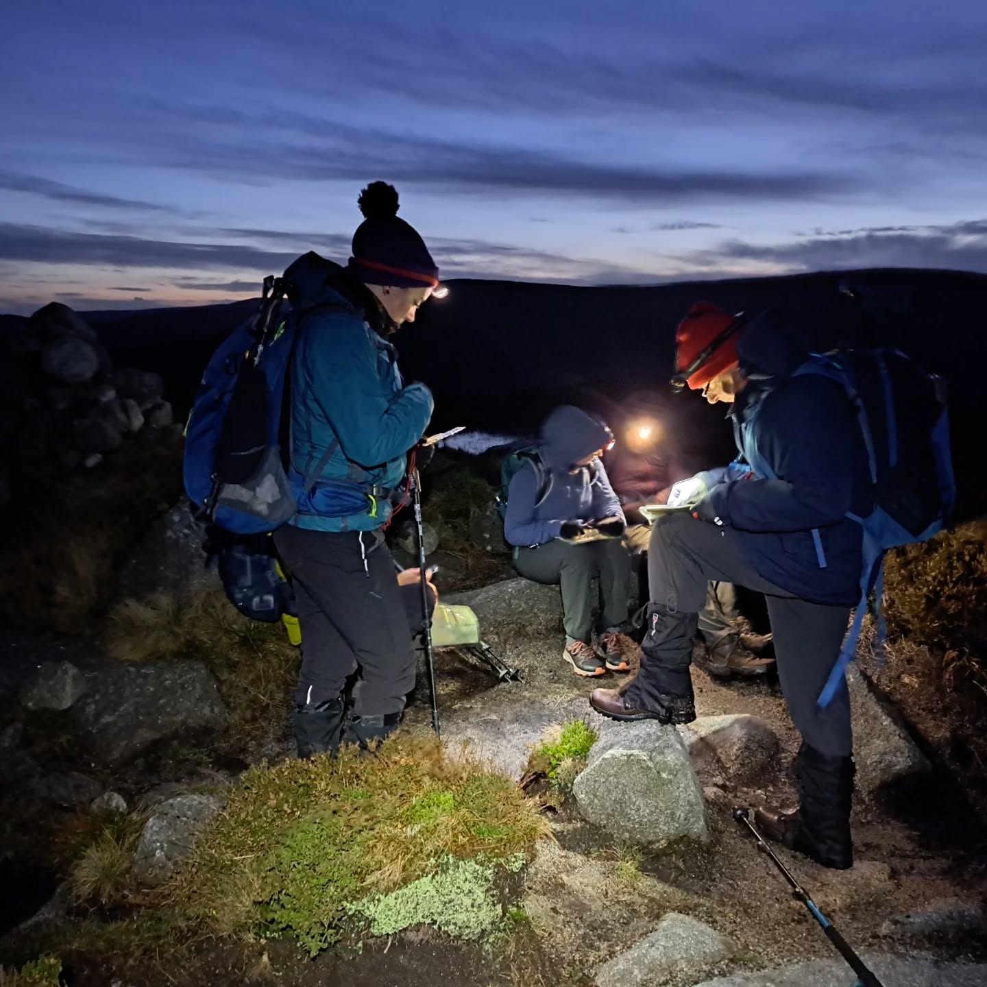Contour Interpretation. Hikers with headlamps read maps on a rocky trail at dusk.
